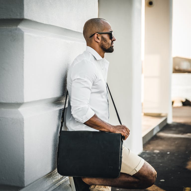 Photo of a Man with a Black Bag Leaning on a White Surface