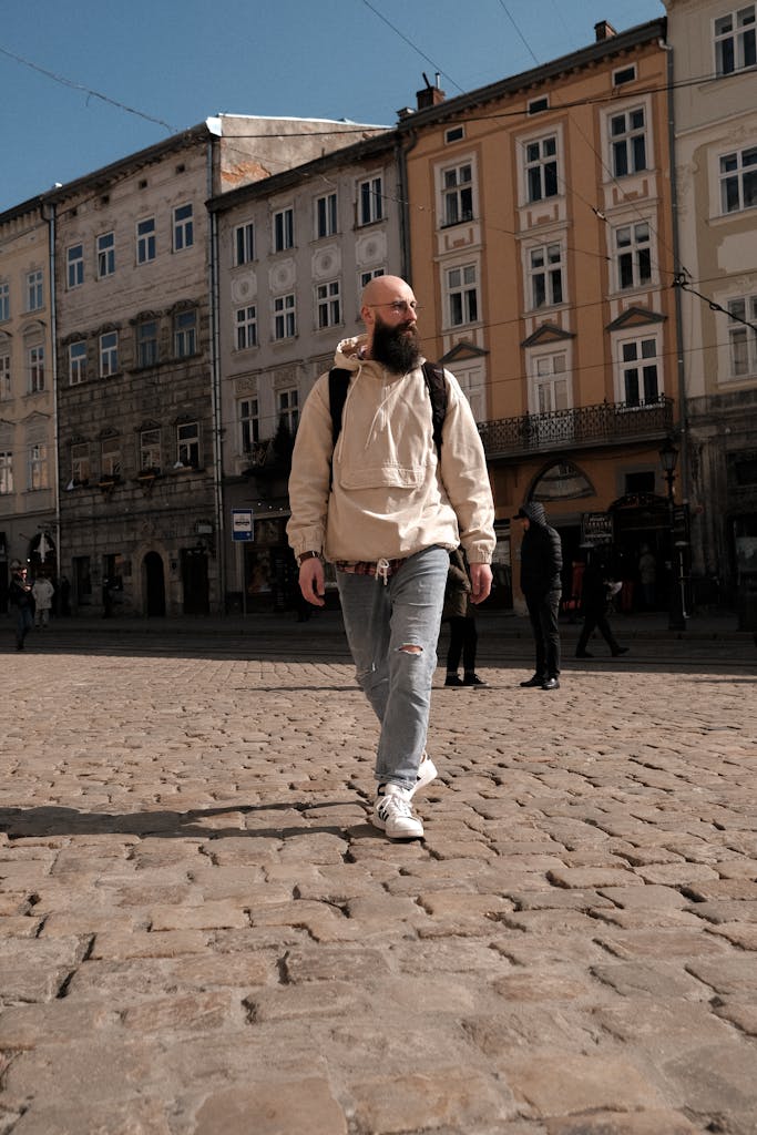 Confident bearded man with backpack on city street near buildings